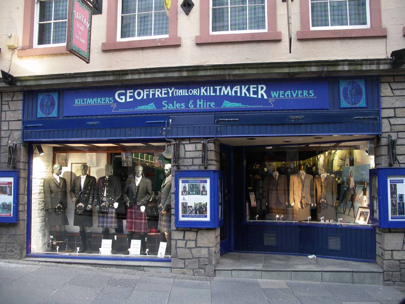 two men in kilts and jackets outside a clothing shop