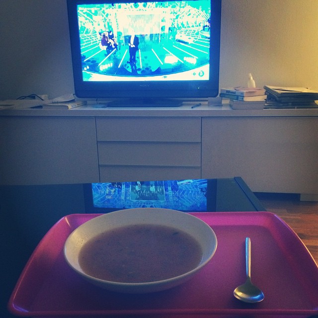 a bowl of soup and spoon on the table in front of television