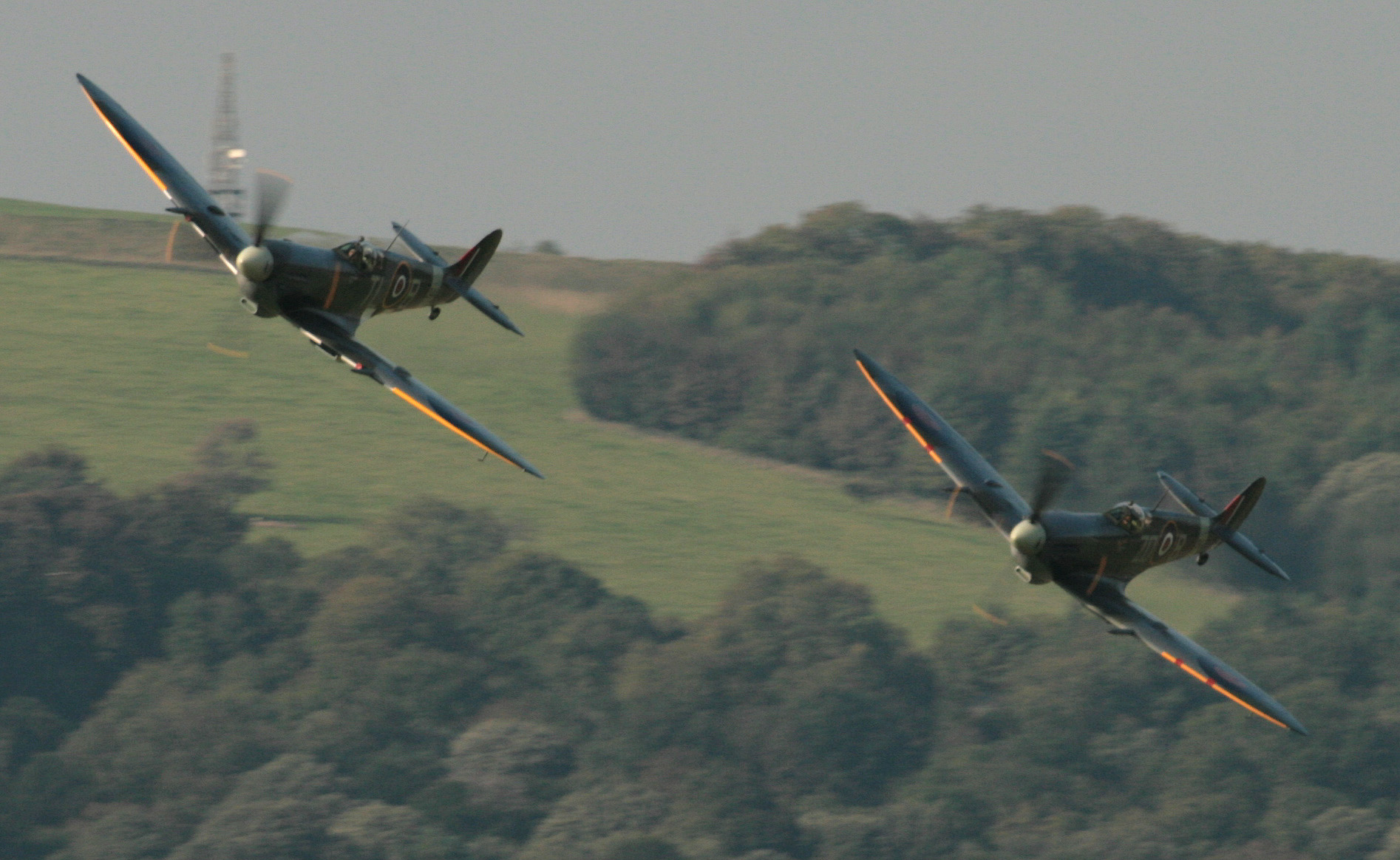 two air planes flying above the ground on a cloudy day