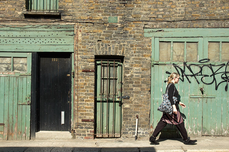 a woman walking past green doors with graffiti on them