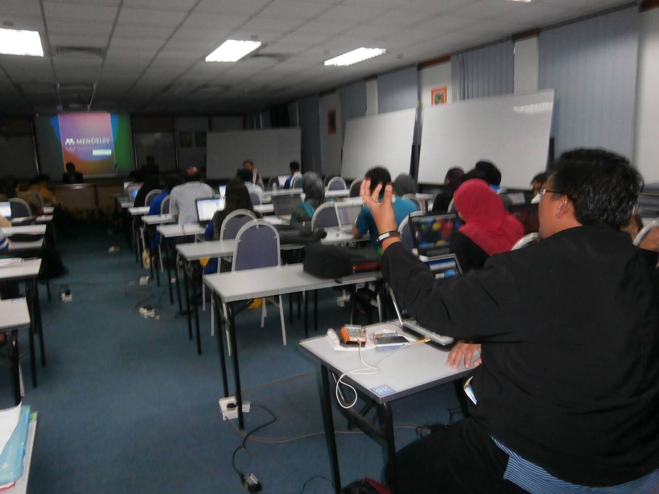 people in an open - air class with one person raising his head and two of them are holding a white board