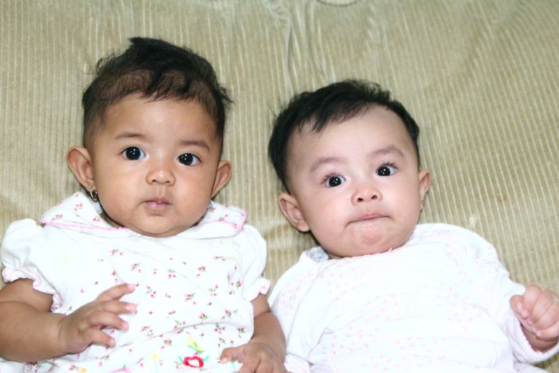 two baby girls looking at the camera, with one looking upward