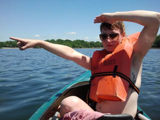 a young woman in an orange life vest and sunglasses paddles on a boat in the water