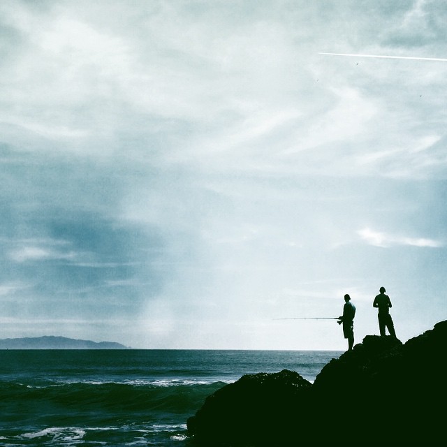 two people standing on a hill near the ocean