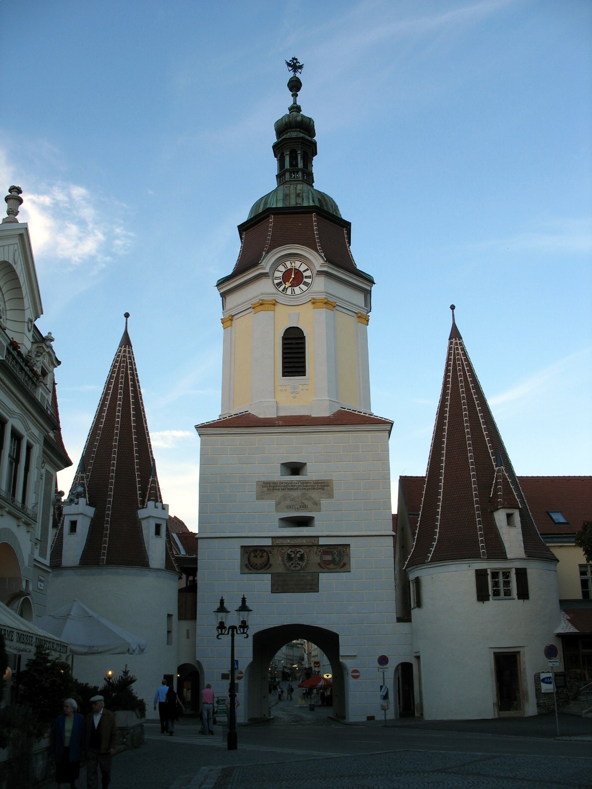 a large tower with two clocks is standing in front of many small buildings