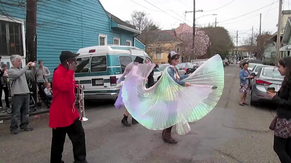 two women and a man in costumes dance on the street while other people walk on the side of the road