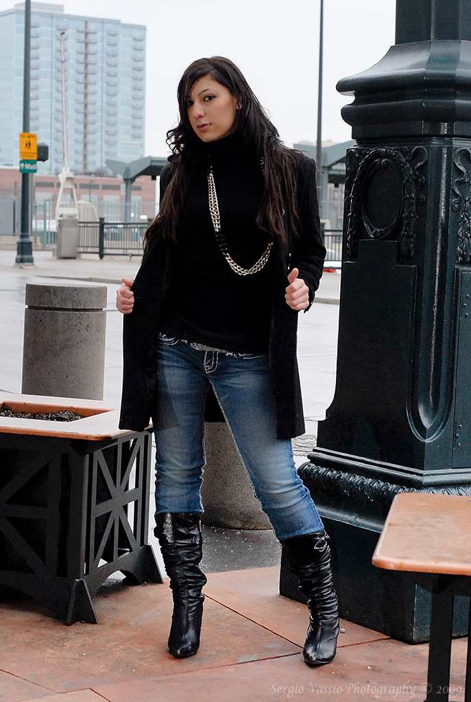 a woman in jeans and boots standing on a sidewalk