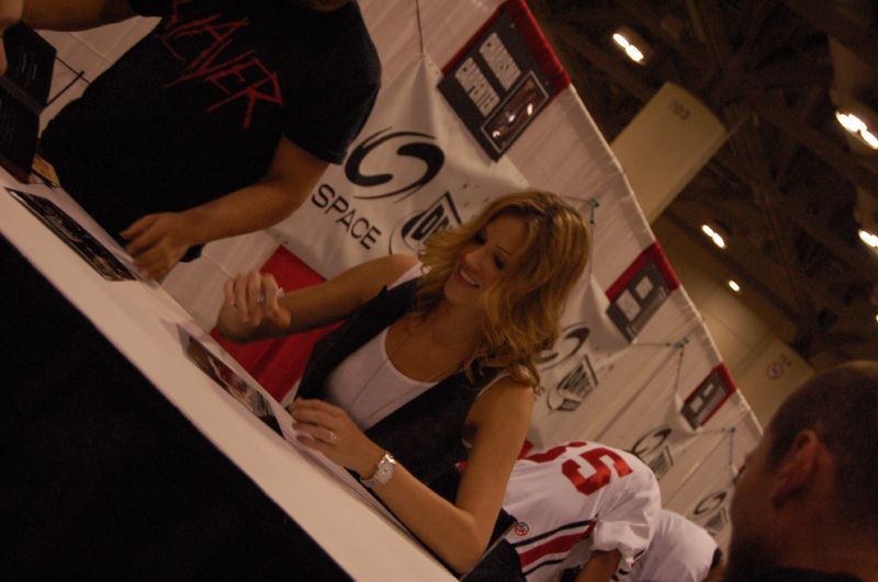 a woman standing at the end of a table signing autographs