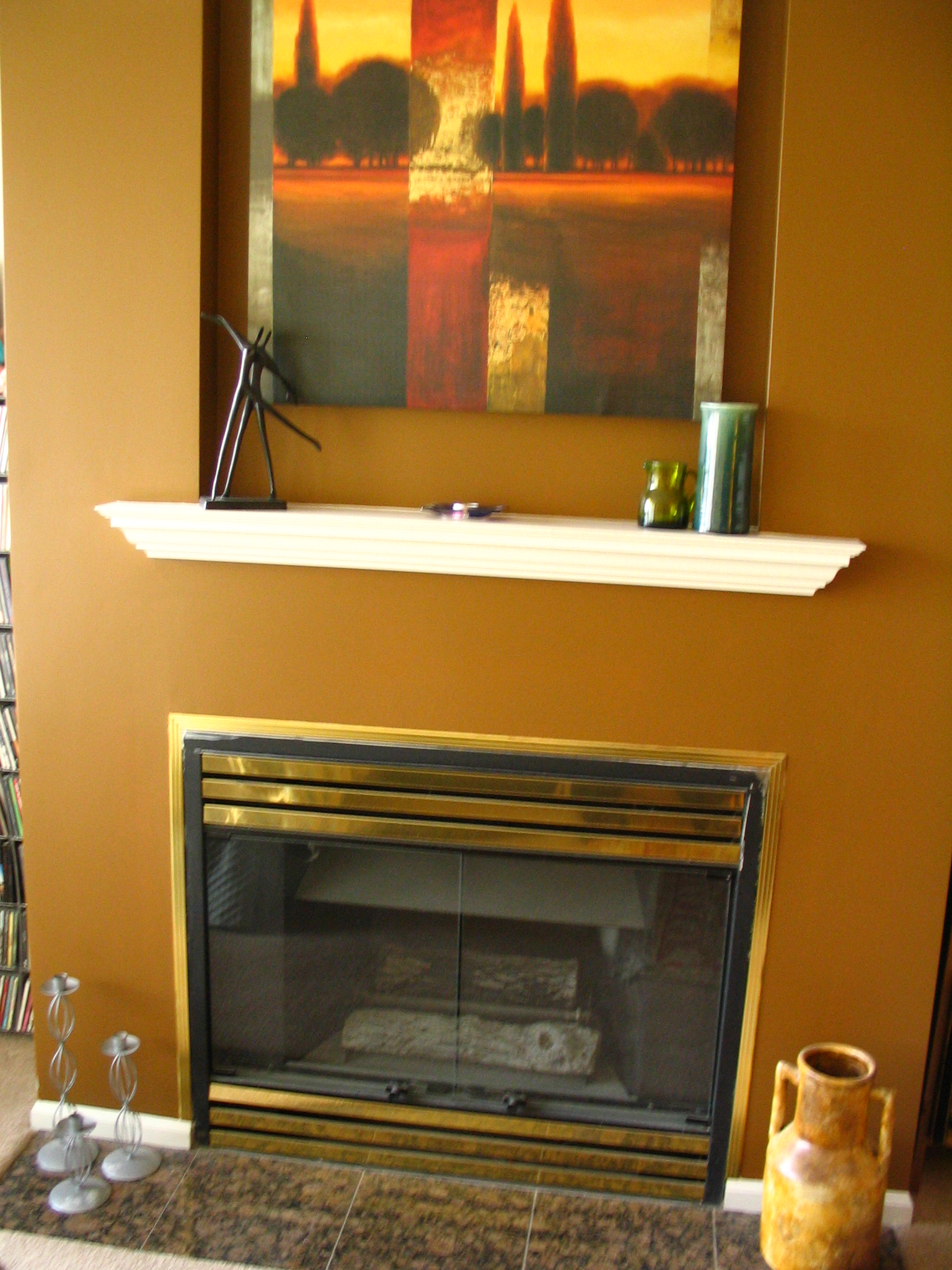 a fireplace with orange walls, large painting on the wall and a painting hanging on the wall above it