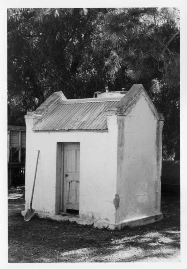 a small white building in front of some trees