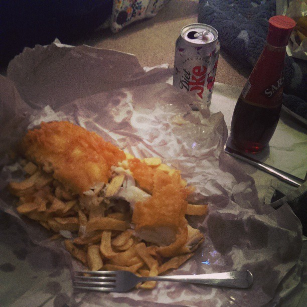 a fish and chips sandwich and drink are on a plate with silverware