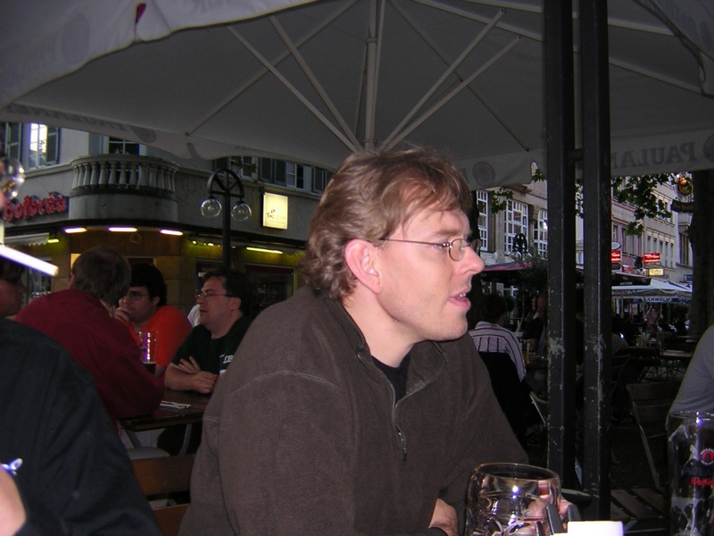 man sitting at a table with an umbrella and wine glass
