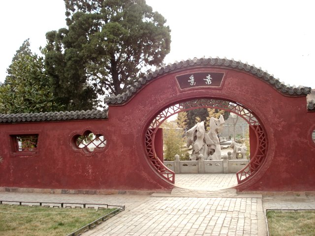 an entrance to the garden that contains statues and a brick walkway