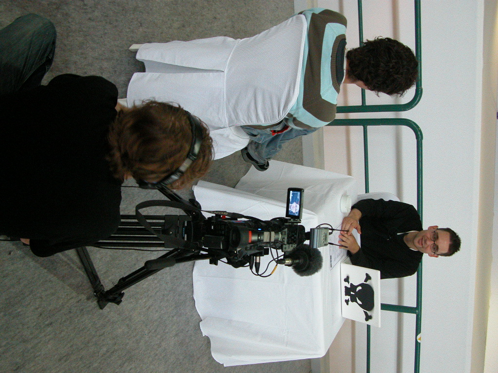 two men in white and black shirts are behind a camera