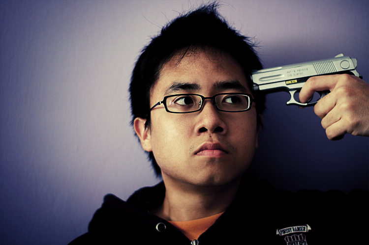 a man with glasses holding a gun on top of his head