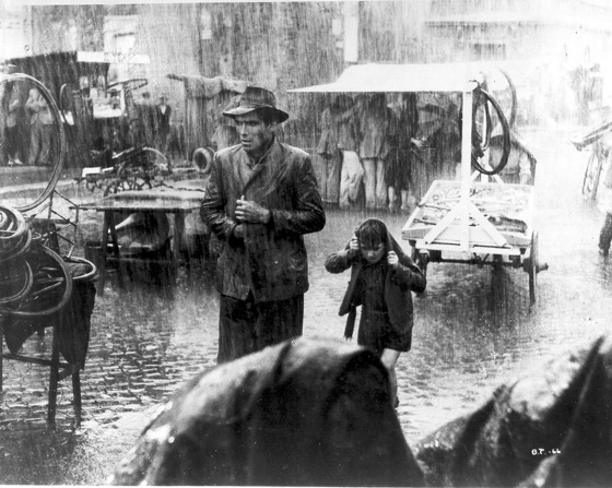 black and white pograph of man and child walking through heavy rain