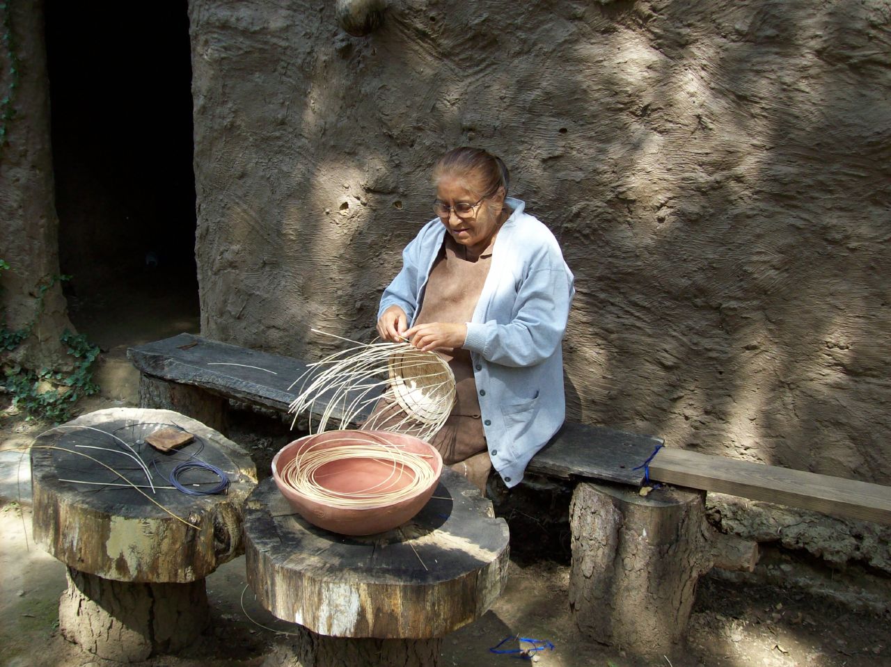 man weaving baskets on wooden benches in a rustic setting