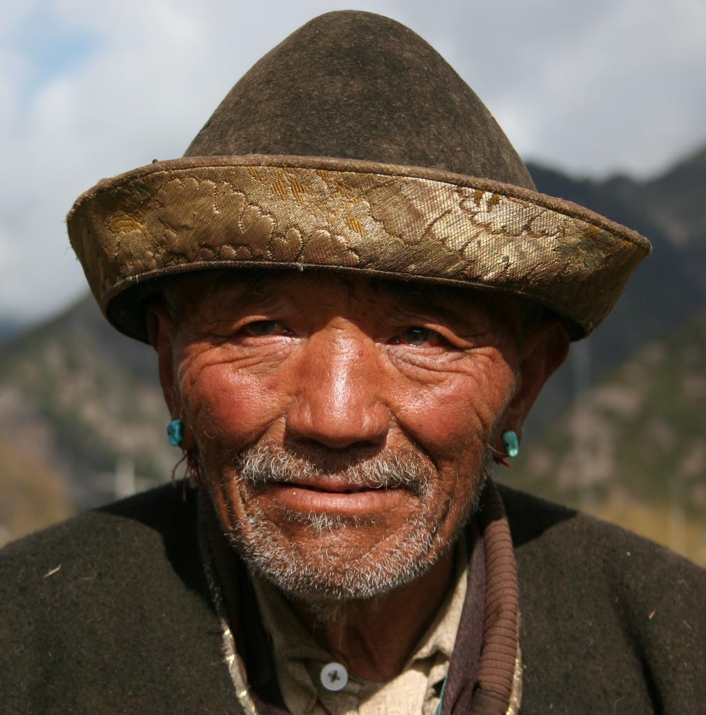 a man with earrings and a hat stands in the mountains