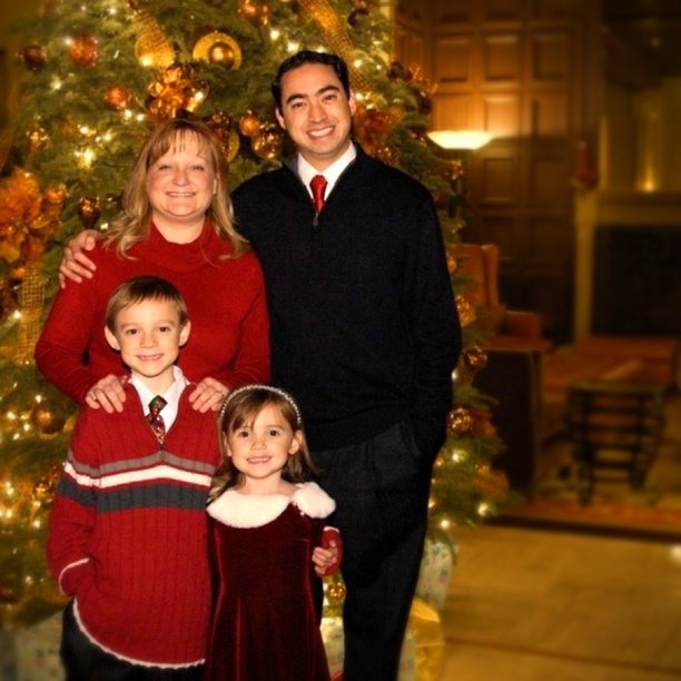 two adults and three children standing next to a christmas tree