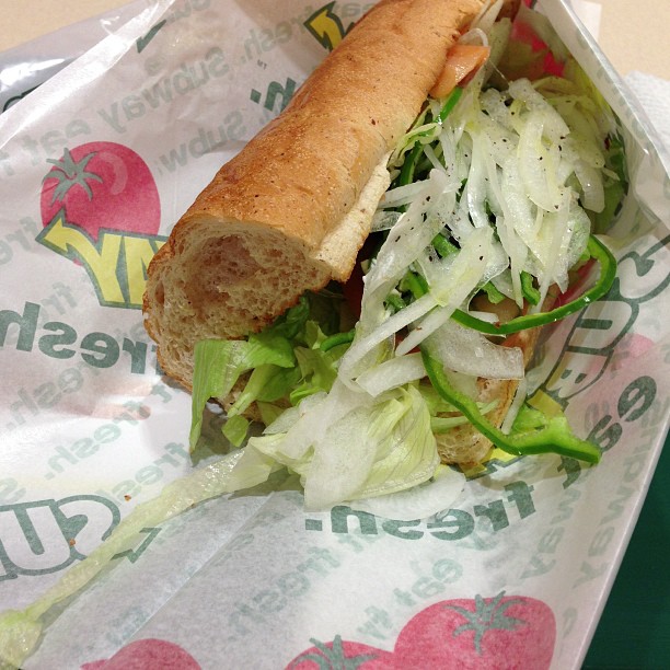 a sub sandwich in paper wrapper with lettuce and tomatoes