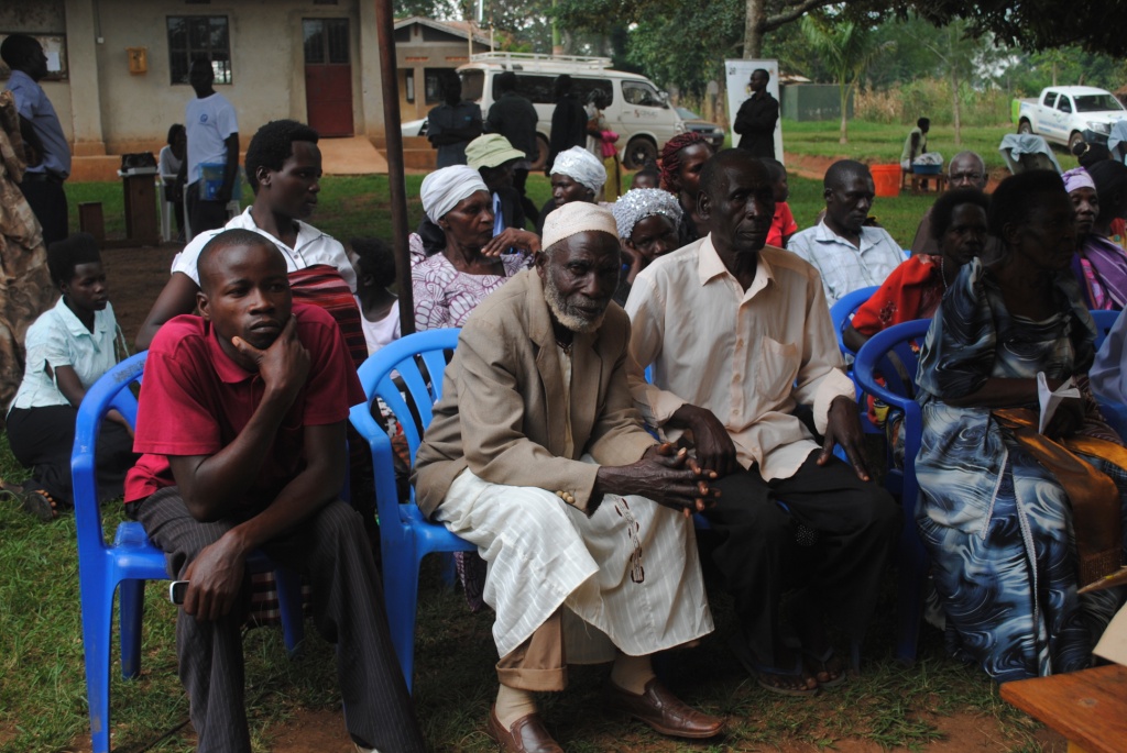 a group of men sitting on chairs outside with many people