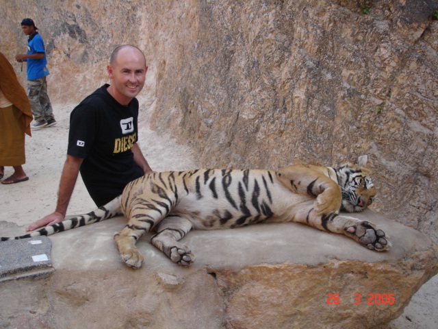 a man poses next to a tiger laying on the ground