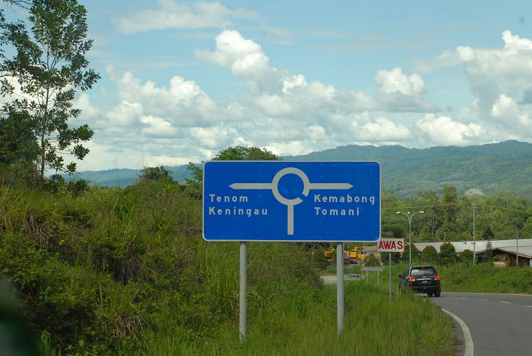 blue and white sign on roadway next to forest