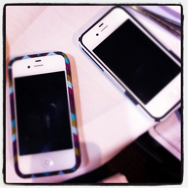 there are two white smart phones, one on a table and one on the desk