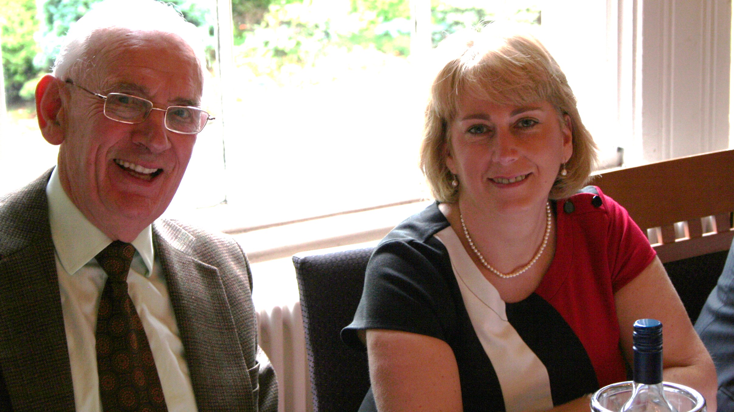 two smiling people seated at a table with wine glasses