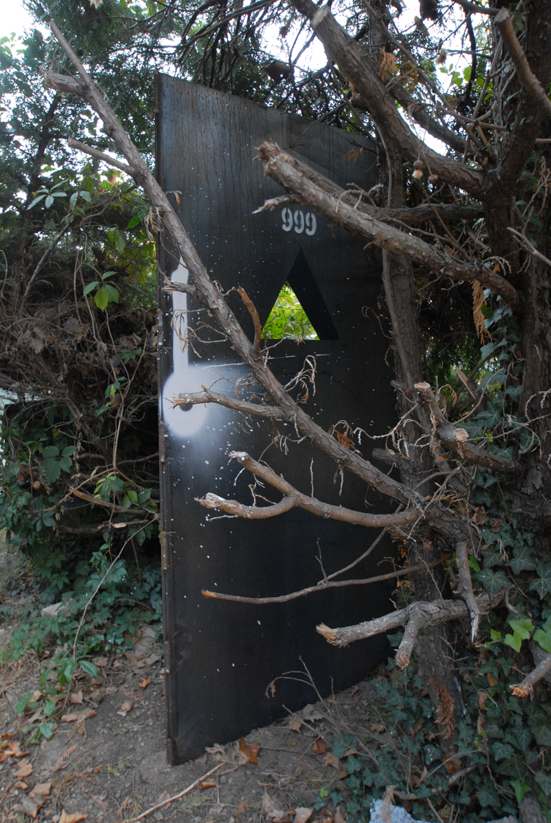 a broken, doored and open black container is surrounded by trees