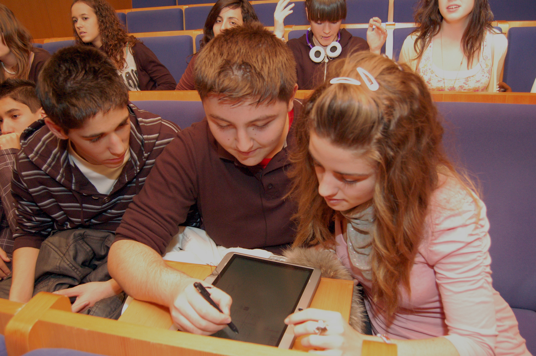 two young children watch as a teacher uses a tablet