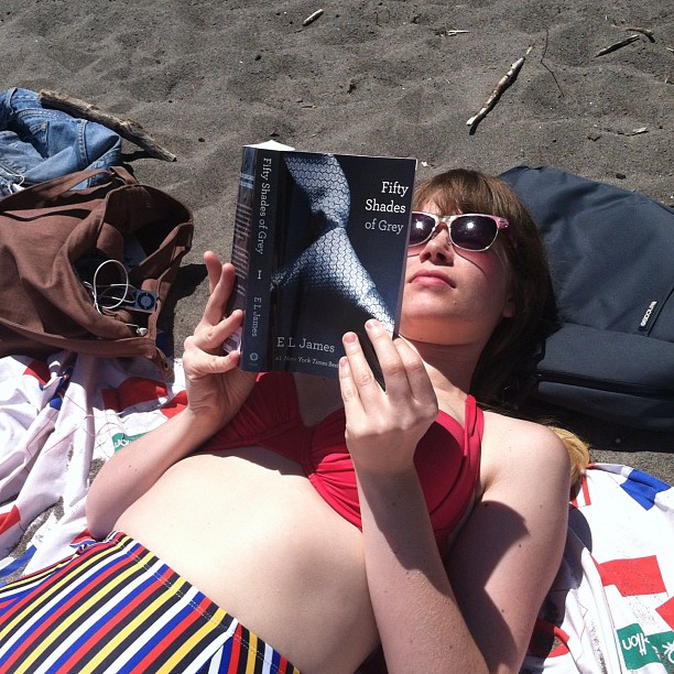 woman sitting on beach chair reading book wearing sun glasses