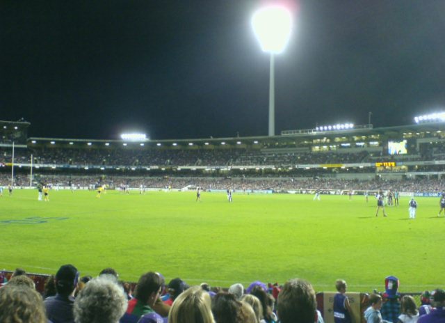 a crowd at a soccer game in front of an illuminated goal field