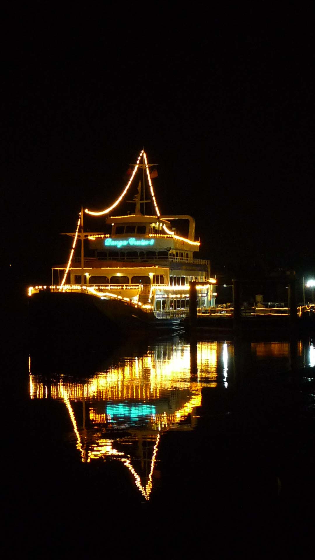 a ship with the christmas lights on sitting next to a pier