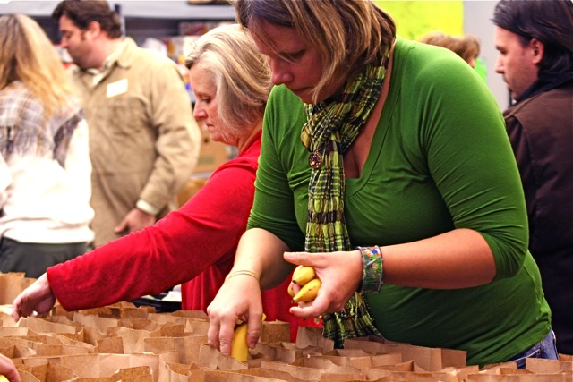 women are picking up fruits from bags at an open market