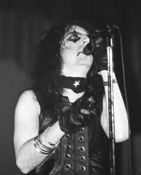 a male singer with black hair and silver makeup, holding a microphone