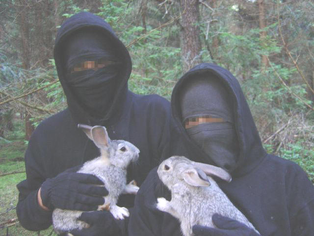 two people in black are holding animals and one is wearing the same bunny costume