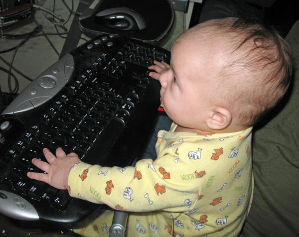 a baby plays with an older computer keyboard