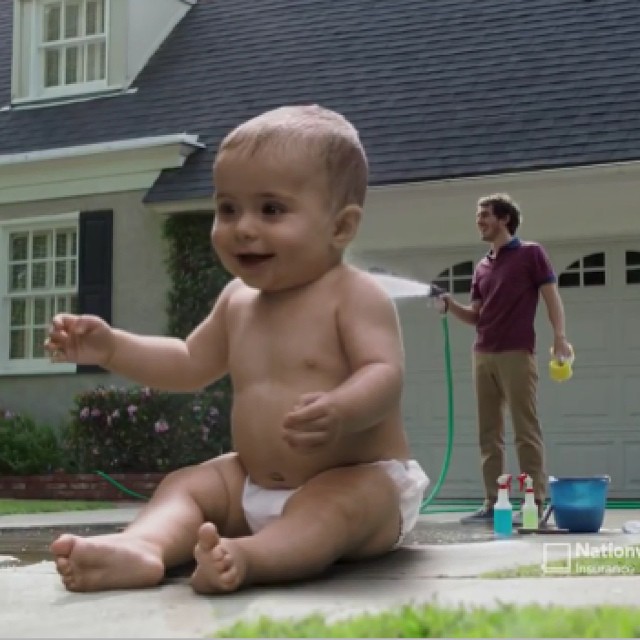 a baby is being soaked with a hose by his dad