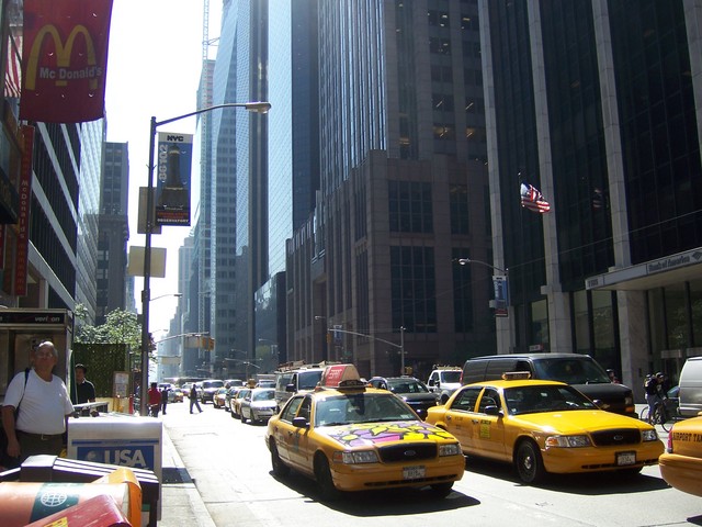 yellow taxi cabs line the street in front of tall buildings