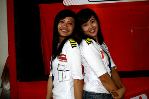 two asian women wearing white shirts posing in front of a red wall