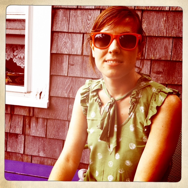 a woman wearing shades sits in front of a house