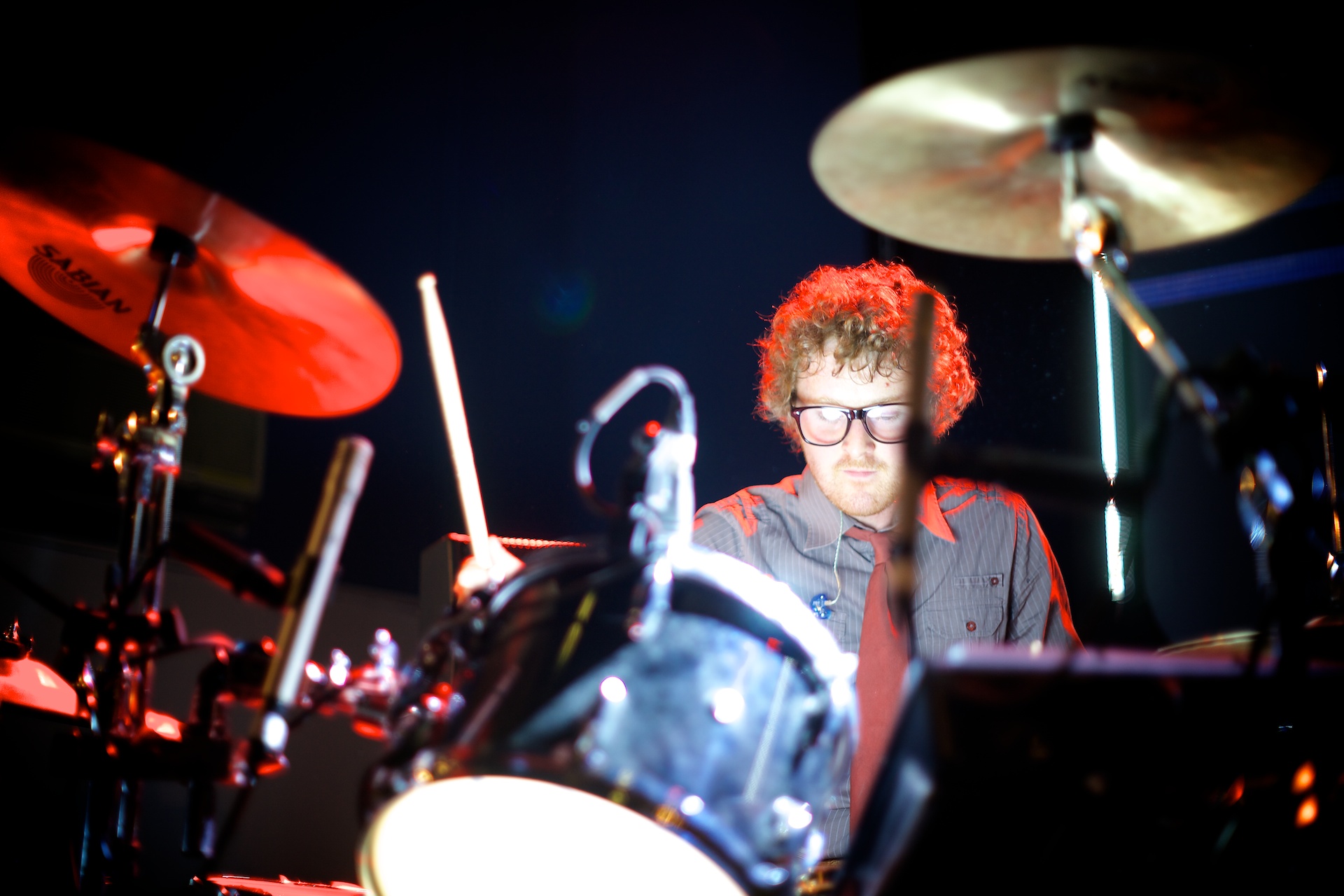 a man wearing eye glasses and a vest playing drums