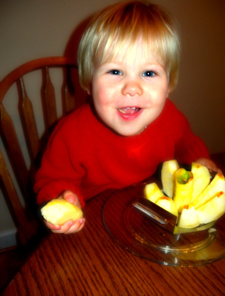 a toddler smiles as he holds up some apples