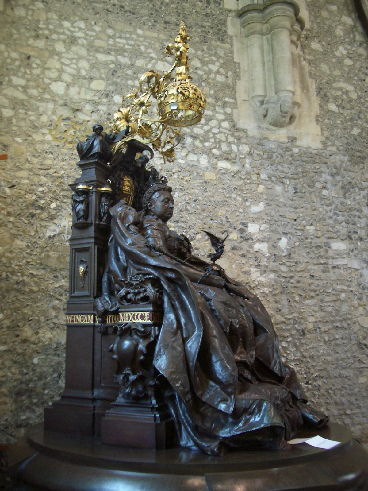 statue of women sitting on an ornate table in front of a brick wall