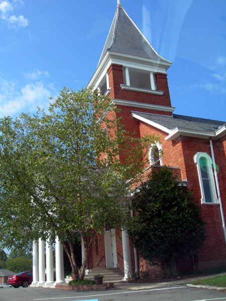 a church steeple with a tall tree in front