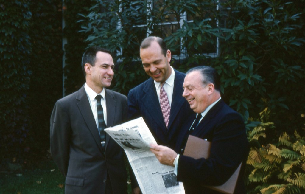 three men standing around each other in suits and ties