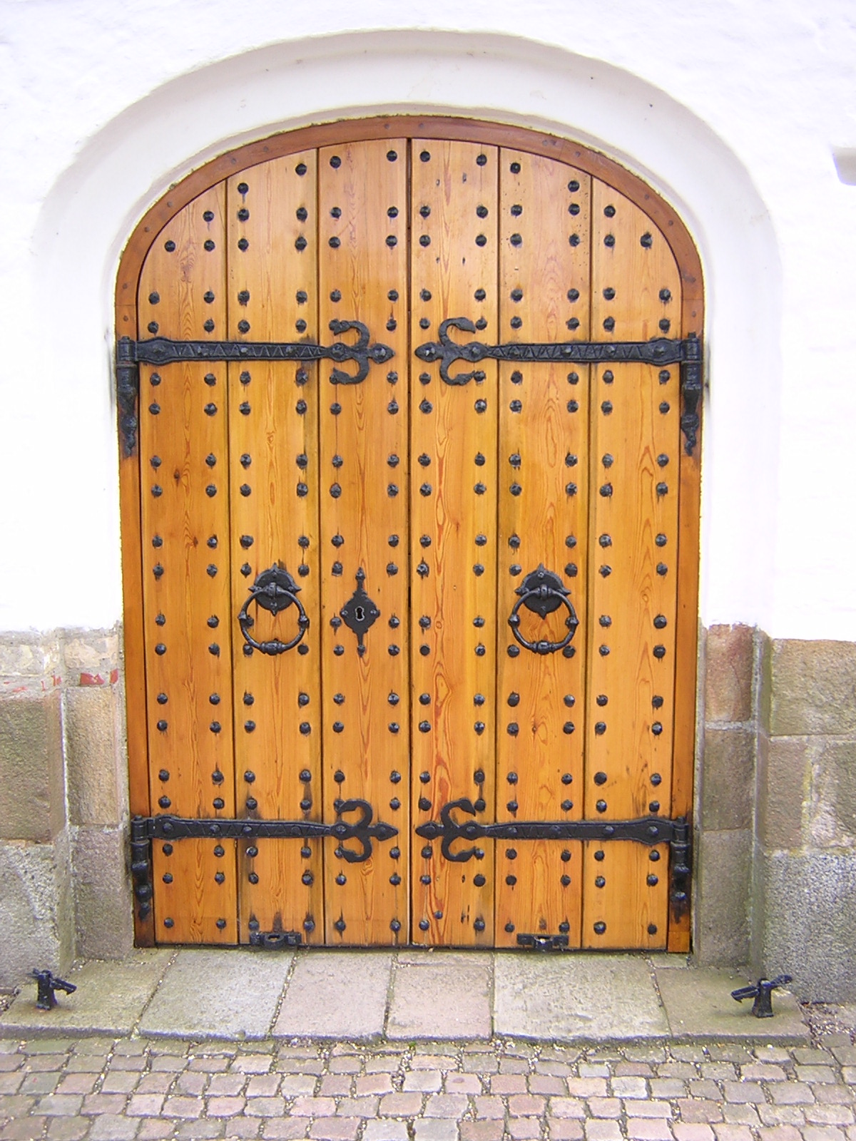 wooden door with decorative hardware on brick walkway