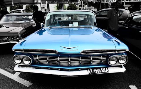 an old blue car sits parked in a parking lot