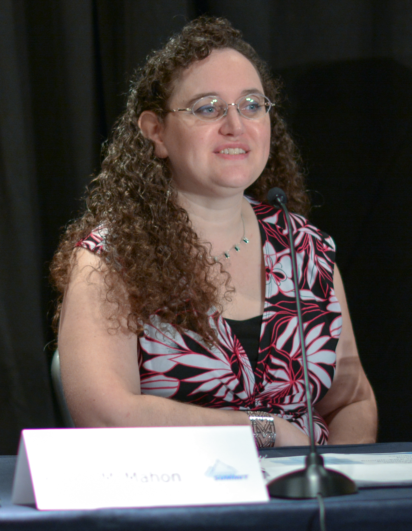 a woman with long brown curly hair speaking at a conference